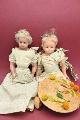 two dolls sitting next to each other on a pink surface