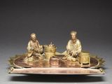 bronze figurines of two men sitting on a tray with a bowl of food
