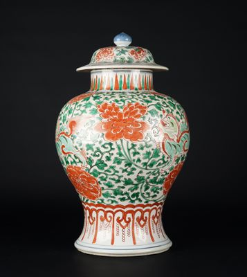 un vase orange et vert muni d'un couvercle, posé sur une surface noire
