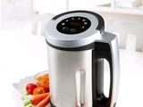 a bowl of soup next to a blender and a bowl of carrots