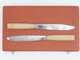 two knives are sitting on a piece of leather on a white surface