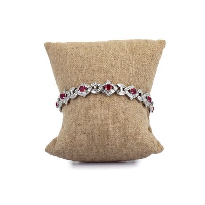 un bracelet en diamants et rubis posé sur un coussin, sur fond blanc