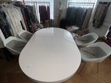 une table et des chaises blanches dans une pièce où sont exposés de nombreux vêtements