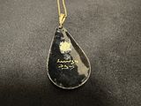 a close up of a black tear shaped pendant with a gold chain