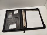 un classeur noir sur lequel sont posés une calculatrice et un bloc-notes