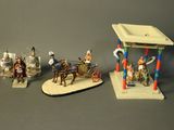 three figurines of people riding horses and a man on a horse drawn carriage