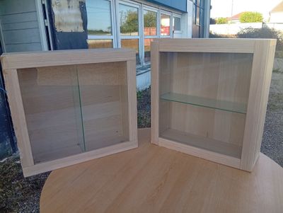 two wooden cabinets with glass shelves on top of a table