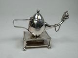 a silver teapot on a stand with a chain around it
