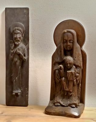 deux sculptures en bois représentant un homme et une femme tenant un enfant dans leurs bras