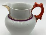 a white pitcher with a red handle sitting on a table