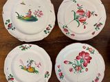 four plates with birds and flowers painted on them on a wooden table