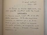 un livre ouvert, sur lequel figure un texte manuscrit, posé sur une table