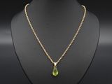 Un collier en or orné d'une pierre verte en forme de larme est suspendu à un mannequin.