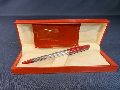 une boîte rouge contenant un stylo, posée sur une surface bleue