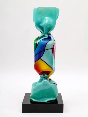 un vase en verre aux couleurs vives posé sur un socle noir, sur fond blanc