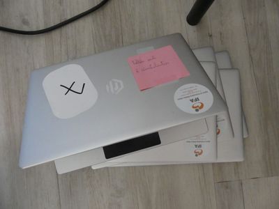 un ordinateur portable recouvert d'autocollants, posé sur une pile de papiers