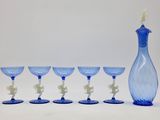 six verres à vin bleus et un vase bleu posés sur une table blanche