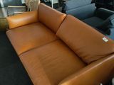 a brown leather couch sitting in a room with other furniture in the background