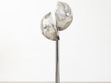 sculpture représentant trois fleurs en argent posée sur un socle métallique devant un mur blanc