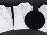 trois paires de pantalons blancs et un chapeau noir posés sur une surface noire