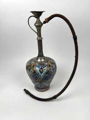un vieux vase argenté et bleu muni d'une poignée en bois, sur fond blanc