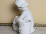 a white statue of a boy sitting on a pot