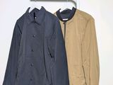 two jackets hanging on a clothes rack against a white wall