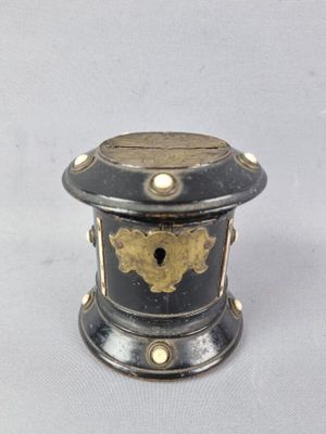 une petite boîte noire et dorée posée sur une surface blanche