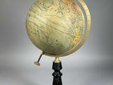 un globe antique posé sur un socle noir, avec un fond blanc