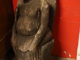 une statue représentant une femme assise sur une chaise près d'un mur rouge