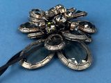 a silver and black flower brooch on a blue surface
