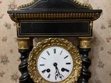 a black and gold clock on a stand against a floral wallpapered wall