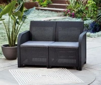 un canapé noir posé sur une terrasse, avec une plante en pot en arrière-plan