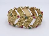 a close up of a gold bracelet with green and red stones
