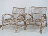 pair of wicker chairs with arms and legs in a white room
