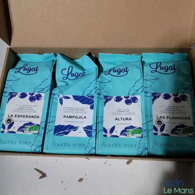 quatre paquets de café sont posés dans une boîte en carton sur une table