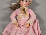 a doll that is sitting on the ground wearing a pink dress and hat