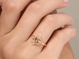 une image représentant la main d'une femme portant une bague en or sertie d'une pierre violette
