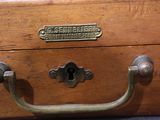 a wooden suitcase with a metal handle and a nameplate on it