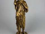 une statue antique en bronze représentant une femme tenant un oiseau, posée sur un socle