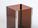 un cube en verre reposant sur un socle métallique, posé sur une surface blanche