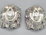 two silver spoons with ornate designs on them sitting on a table