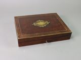 an old wooden box sitting on a white surface with a gold emblem on the lid