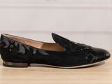 the black loafer is on a wooden table with a white wall in the background