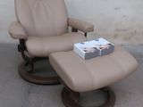 un fauteuil inclinable sur lequel est posé un livre, et une boîte de livres posée sur le pouf