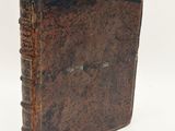 an old brown book sitting on top of a table next to a white wall