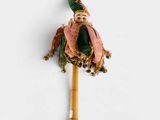 une petite poupée avec un chapeau vert et une écharpe rose, fixée sur un bâton