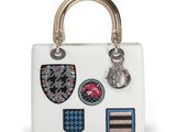 a white handbag with patches and a metal handle on a white background