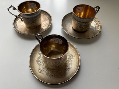 three silver cups and saucers on a white table