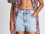 a woman in a floral top and denim shorts stands in front of a white background